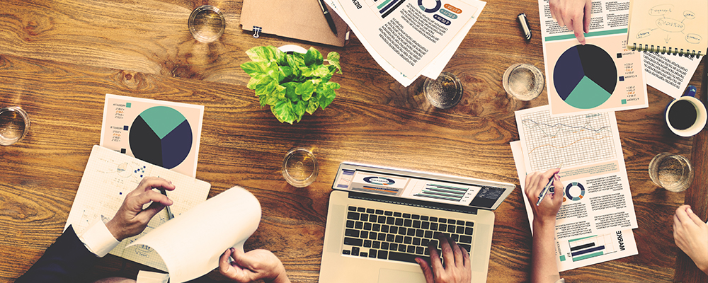 A group at a table with charts, documents, a laptop discussing healthcare marketing