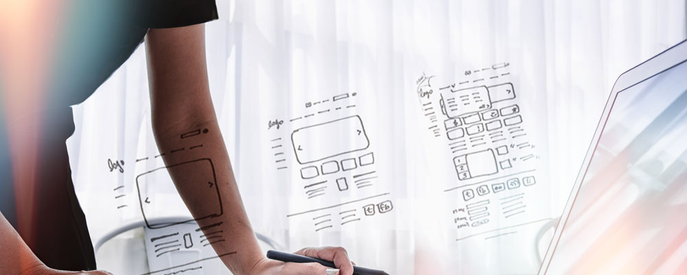 Person writing on a digital tablet with website layout sketches overlaid.