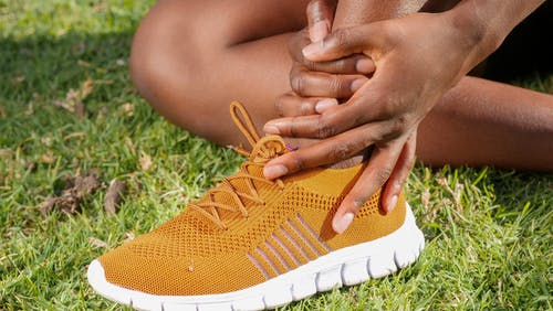 A person sitting on the grass while wearing an athletic shoe highlighting podiatry advertising.