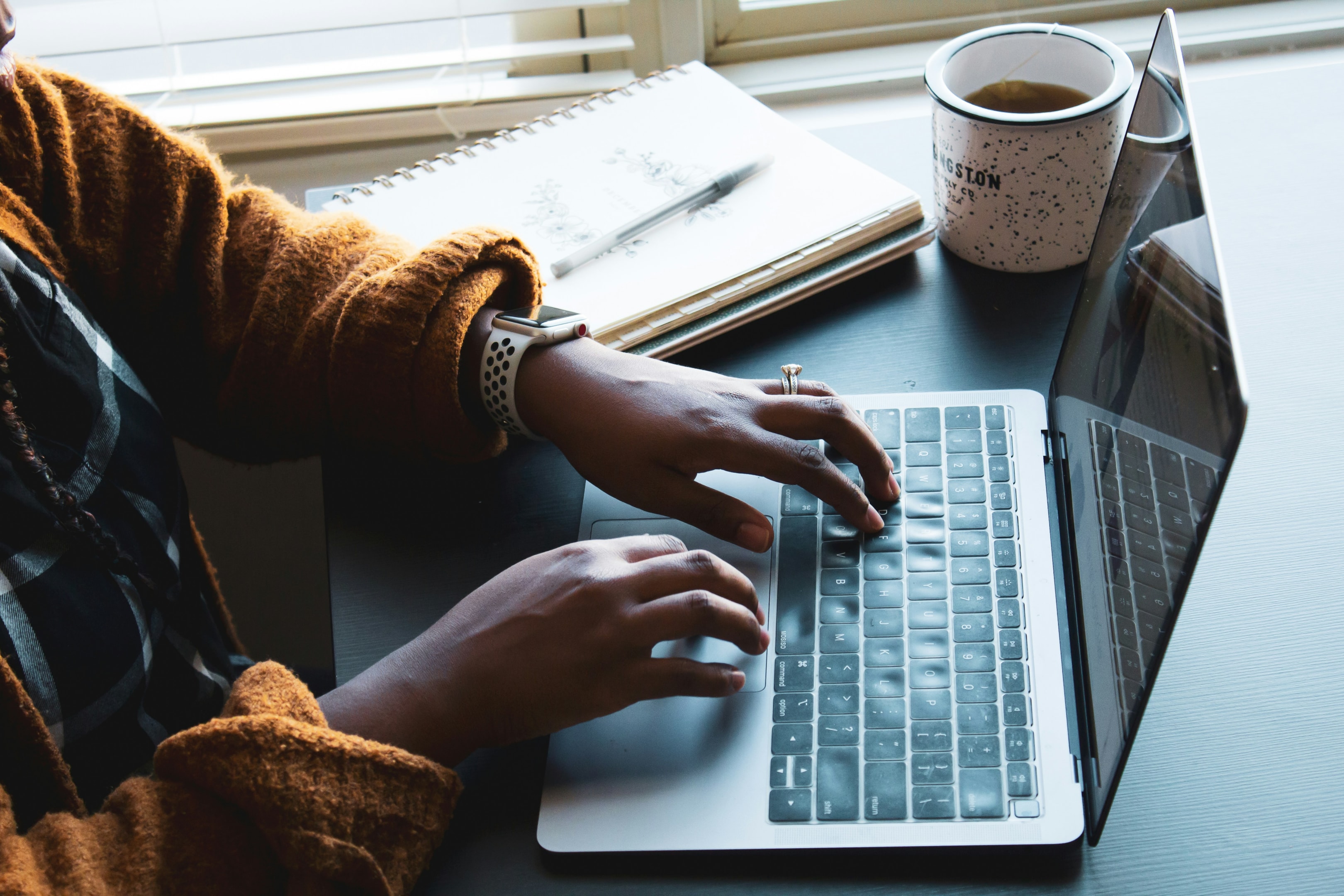 Person typing on a laptop beside a notebook and a mug delivering reputation management.